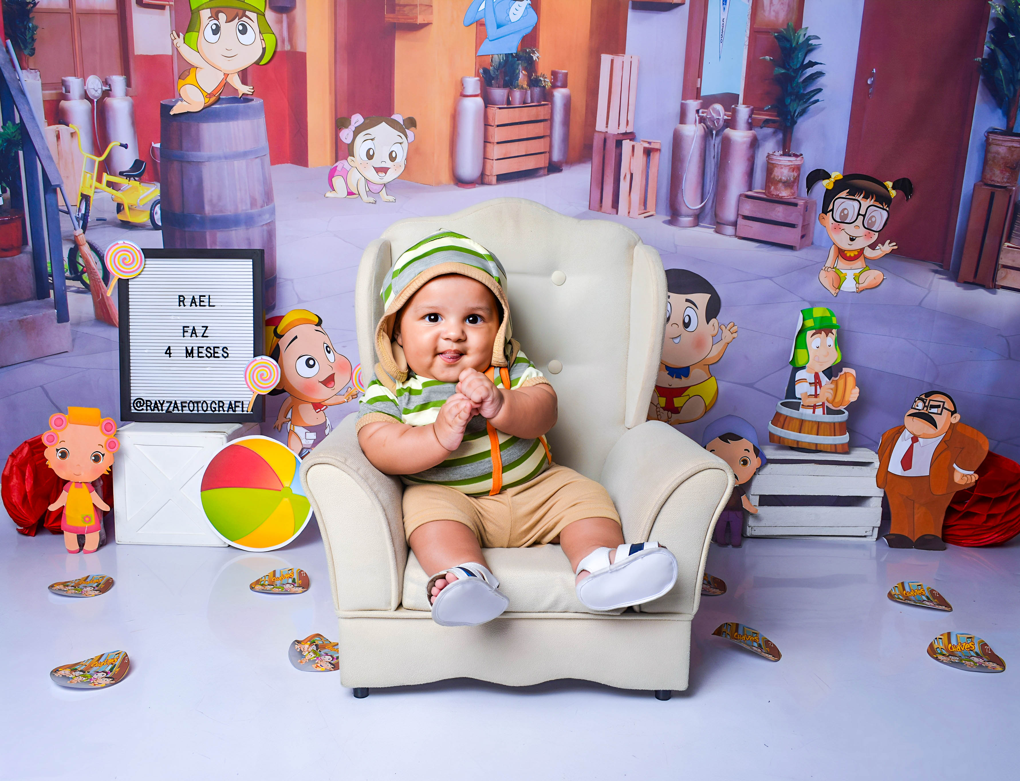 Bebê com touca verde sentado em uma poltrona, envolto em um cenário colorido com personagens infantis.