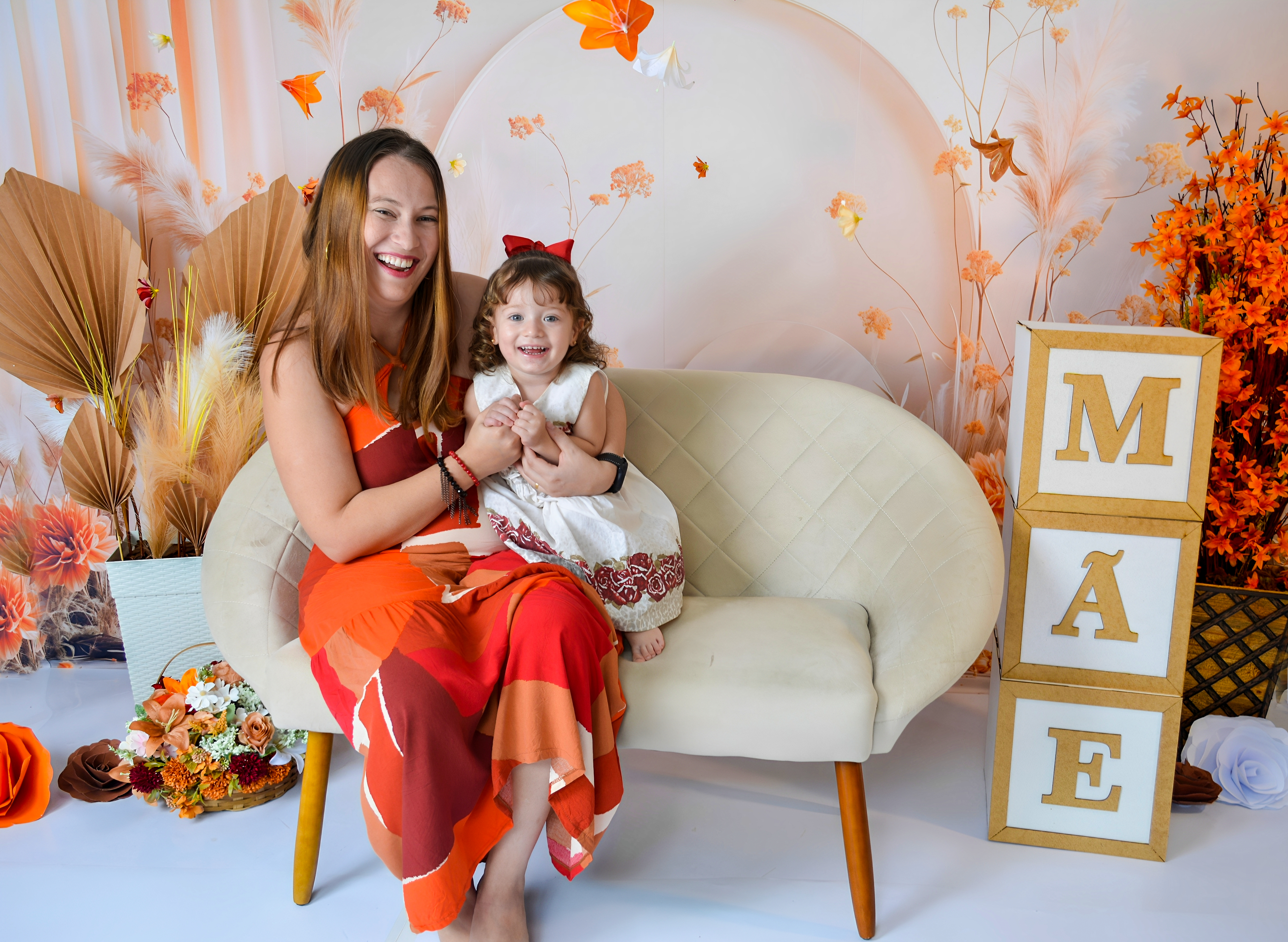 Mãe e filha sorrindo juntas ao lado de caixas que formam a palavra 'MÃE', em um ensaio fotográfico especial.