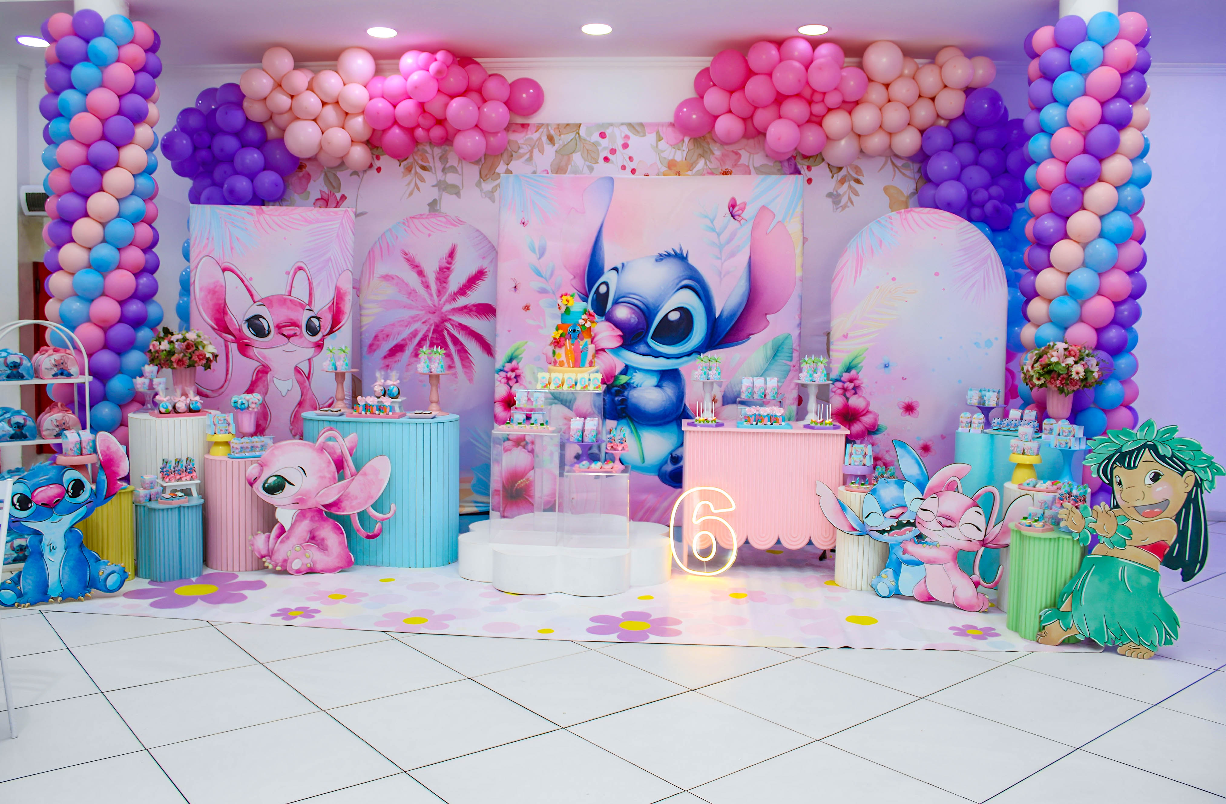 Menina sorrindo diante de um painel decorado com o personagem Stitch e balões coloridos, em festa infantil.