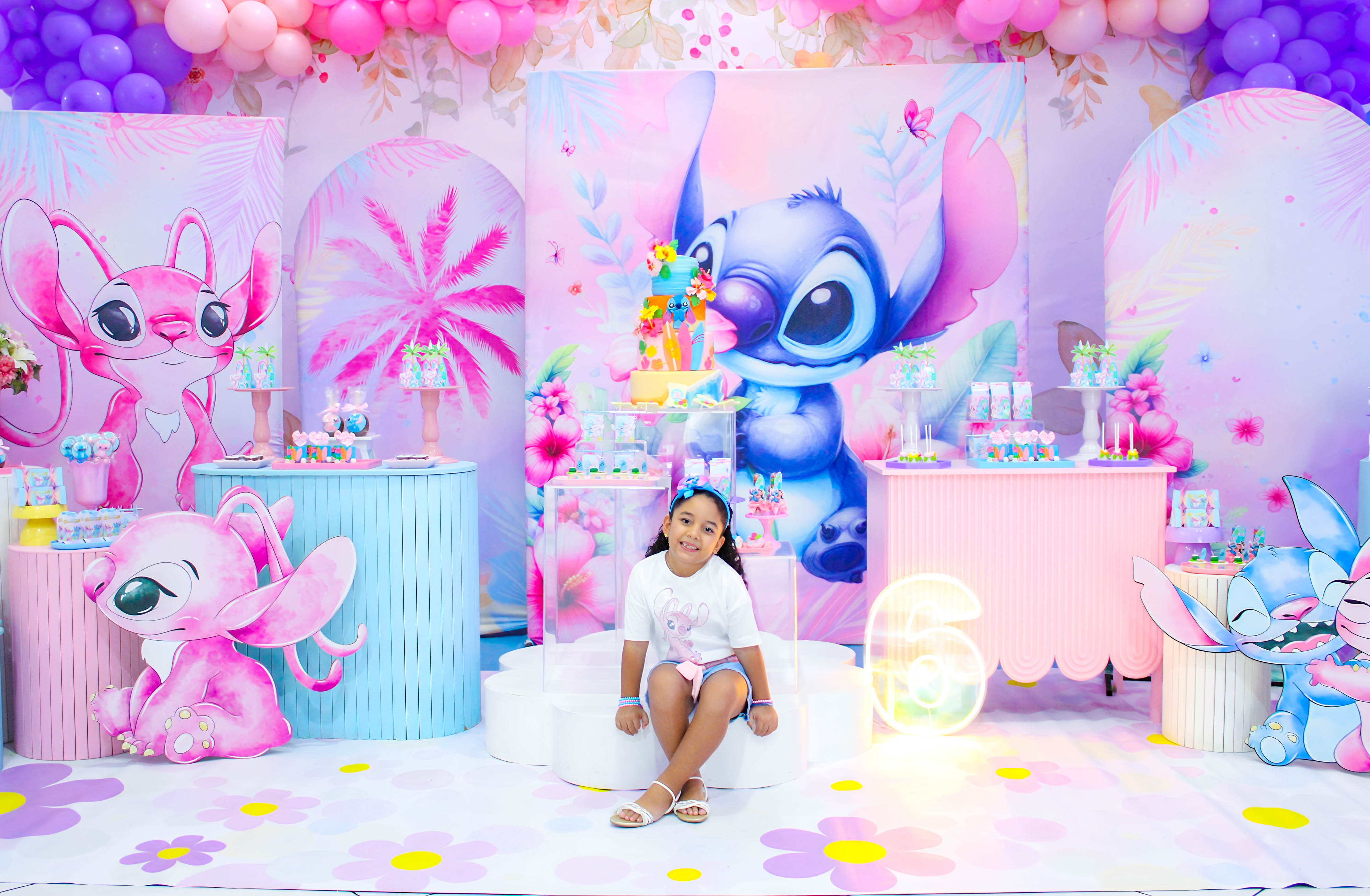 Família posando ao lado da aniversariante em frente a um cenário com o personagem Stitch e balões cor-de-rosa.