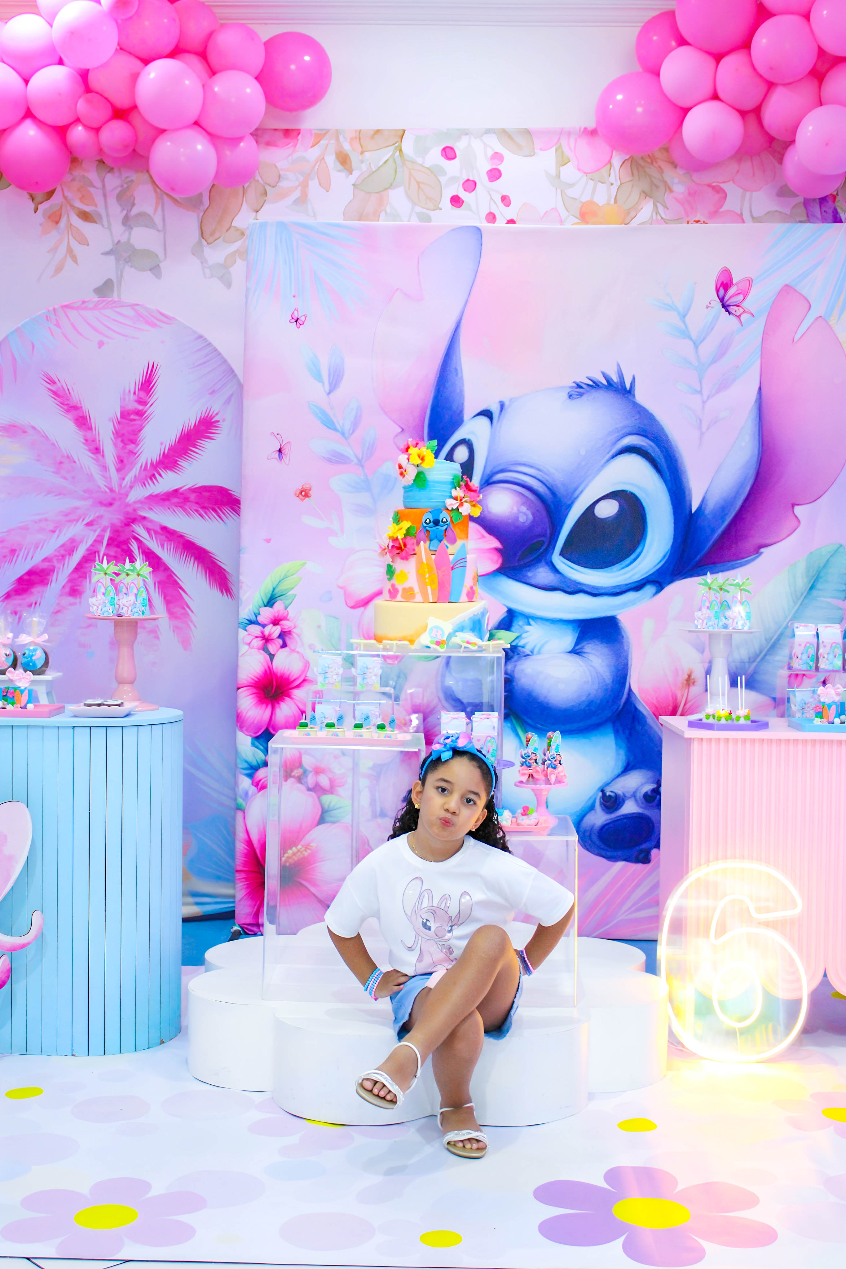 Menina vestindo camiseta branca posando com os pais, em um ambiente de festa infantil com tema Lilo & Stitch.