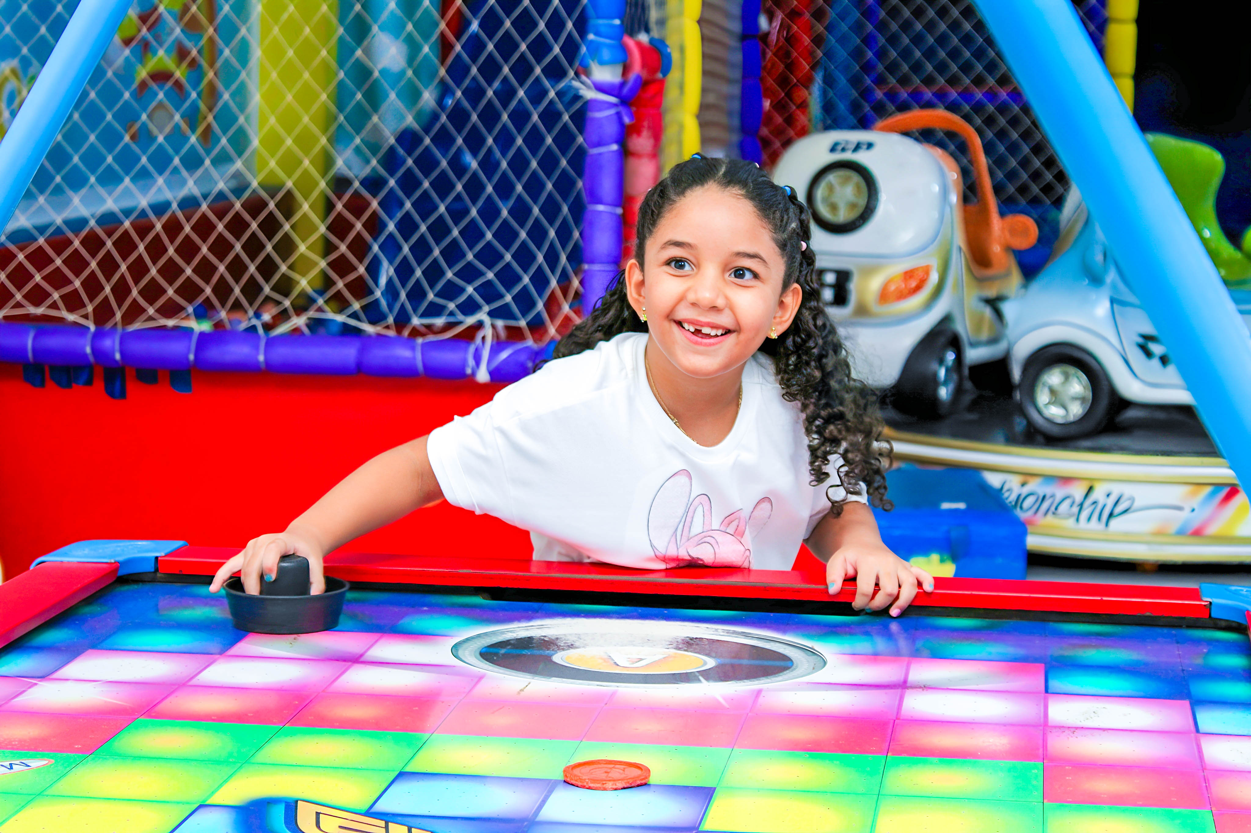 Menina se divertindo em um brinquedo interativo, cercada por elementos de uma festa infantil no tema Stitch.