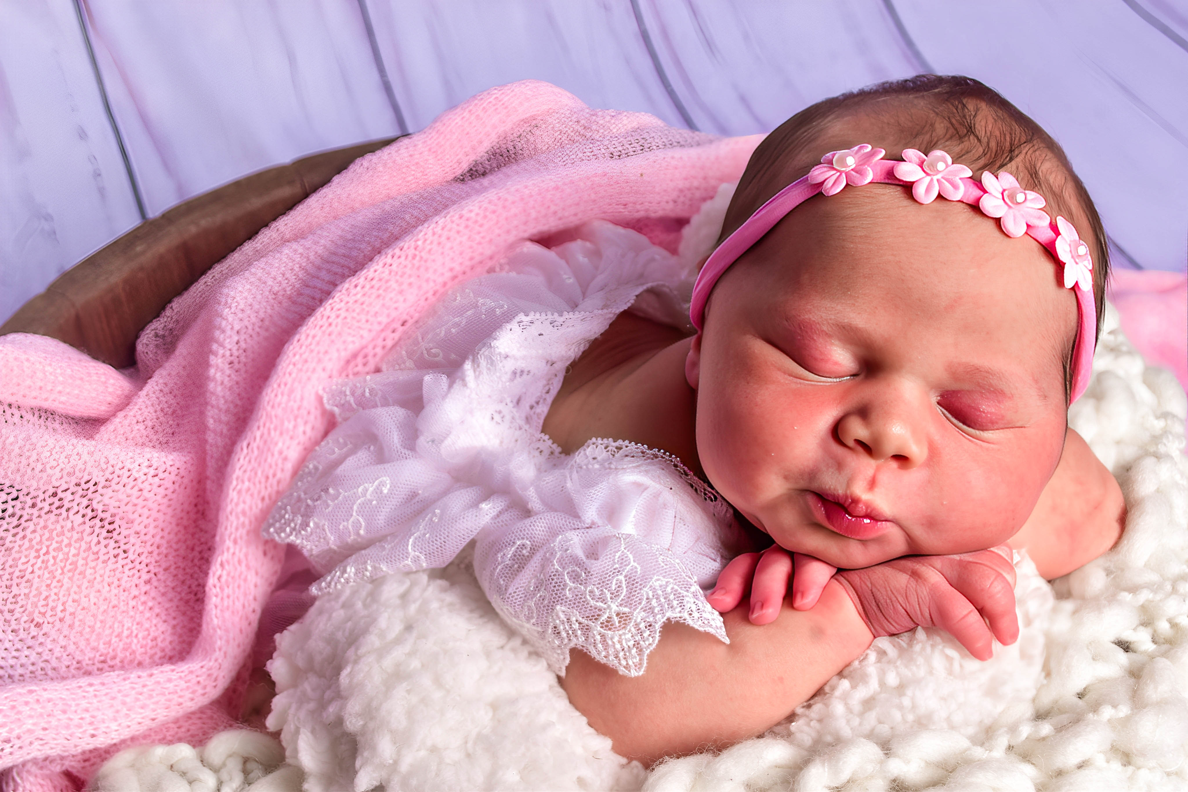 Recém-nascida usando vestido e manta rosa, dormindo em um ensaio newborn.